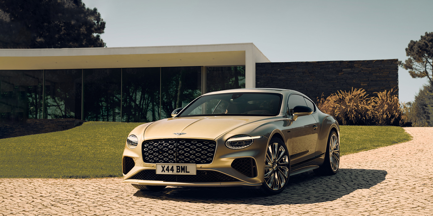 Bentley Taipei Bentley Continental GT Mulliner coupe front three quarters in Patina paint parked outside a glass fronted building with a grass lawn behind it