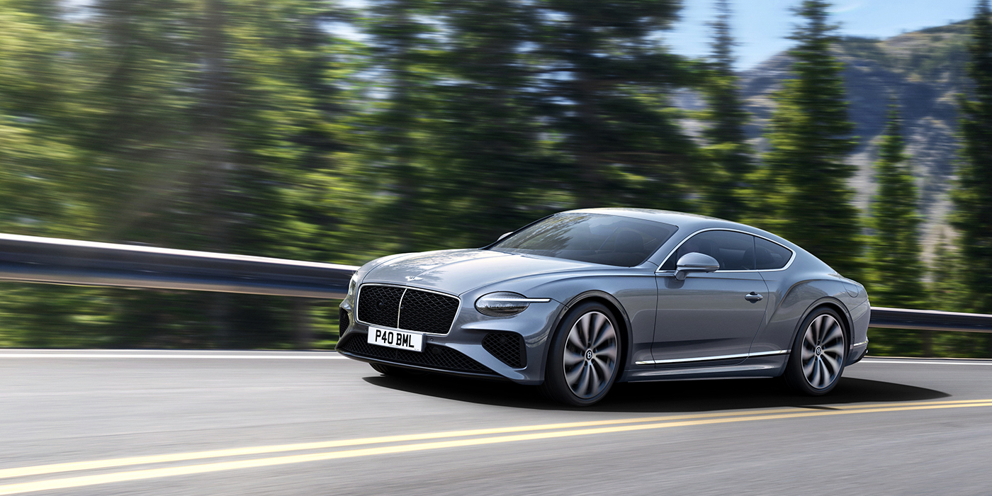 Bentley Taipei New Bentley Continental GT coupe in Silverlake paint and 22 inch ten-spoke wheels, driving dynamically on a tree-lined road in the sunshine