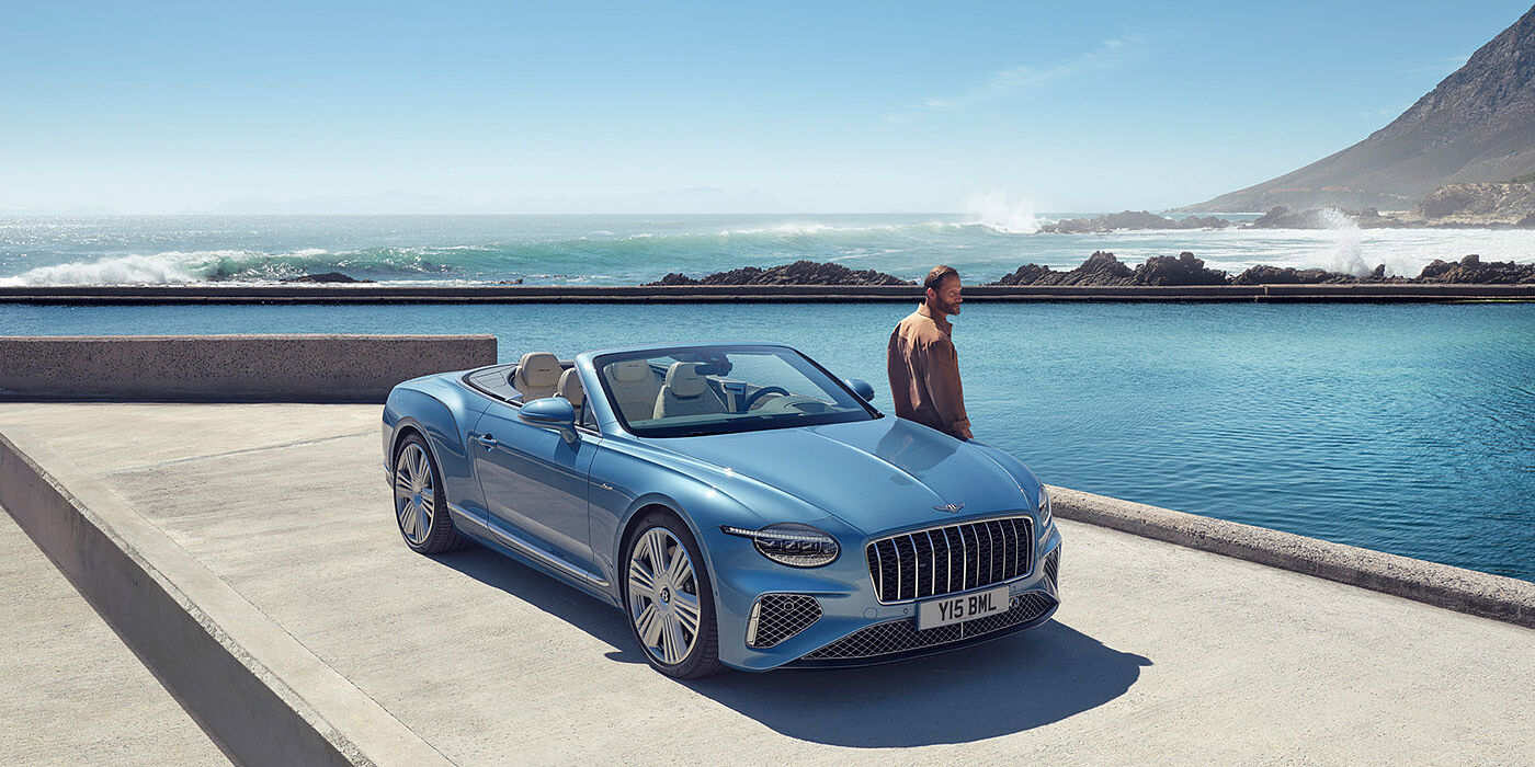 Bentley Taipei New Bentley Continental GTC Azure convertible front view in Light Windsor blue paint with 22 inch ten spoke wheels parked by the sea in the sunshine
