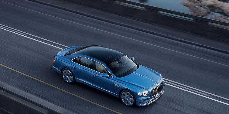 Bentley Taipei New Bentley Flying Spur Azure sedan in Light windsor blue paint by Mulliner, with 22 inch Azure wheels seen from overhead driving dynamically on a country road