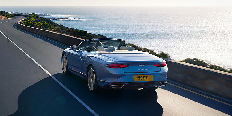 Bentley Taipei New Bentley Continental GTC Azure convertible rear view in Light Windsor blue paint with 22 inch ten spoke wheels driving dynamically on an ocean road in the sunshine
